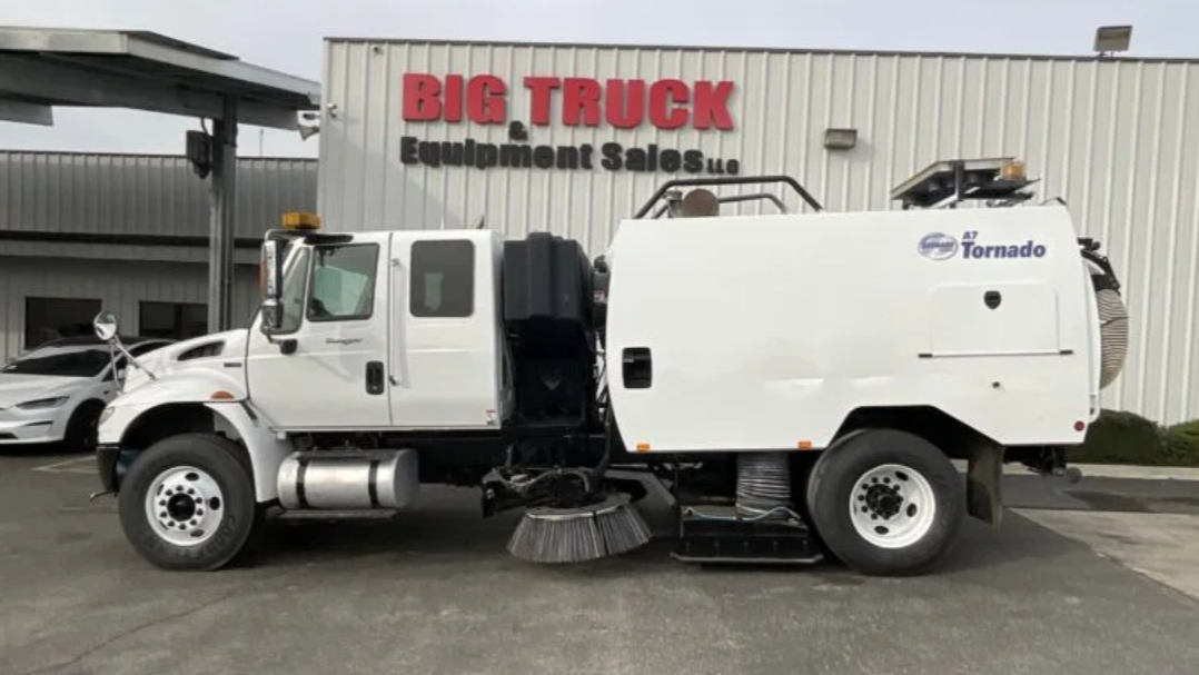 Side view of a white municipal street sweeper truck